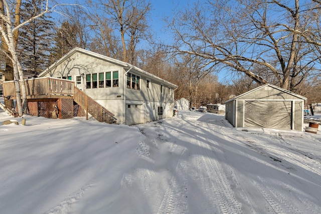 view of snow covered exterior with a garage, stairs, a deck, and an outbuilding