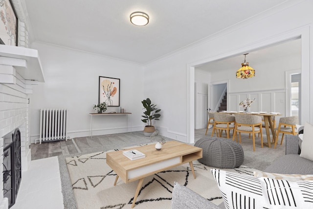 living room featuring radiator heating unit, stairway, crown molding, a brick fireplace, and a decorative wall