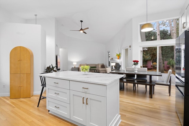 kitchen with white cabinetry, decorative light fixtures, black refrigerator, and light stone countertops