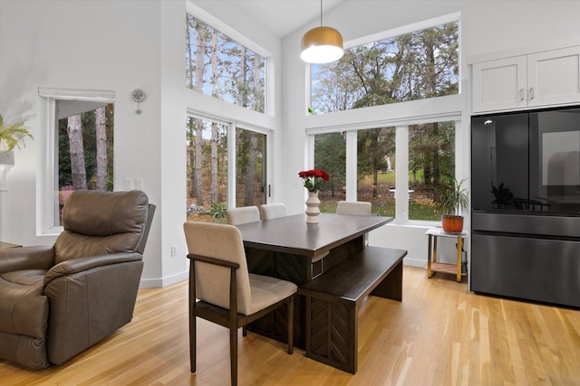 dining space with light hardwood / wood-style flooring, a healthy amount of sunlight, and a high ceiling