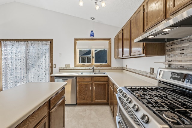 kitchen with lofted ceiling, under cabinet range hood, a sink, light countertops, and appliances with stainless steel finishes