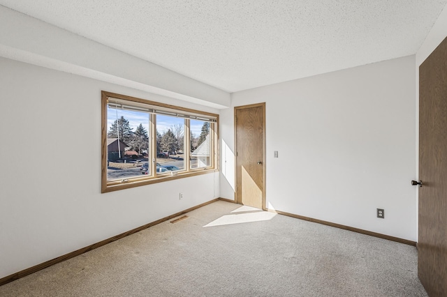 unfurnished room with a textured ceiling, carpet flooring, visible vents, and baseboards