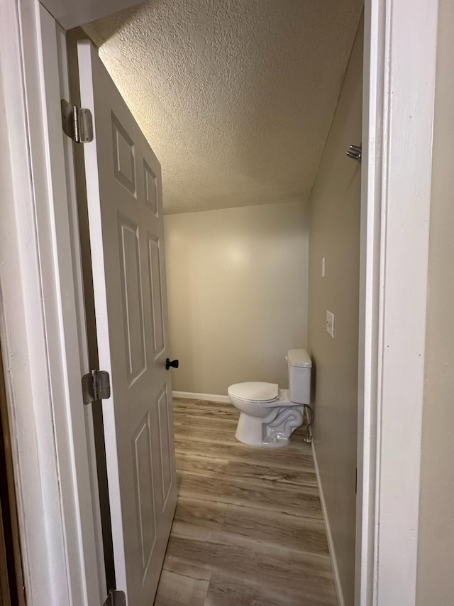 bathroom with a textured ceiling, wood finished floors, toilet, and baseboards