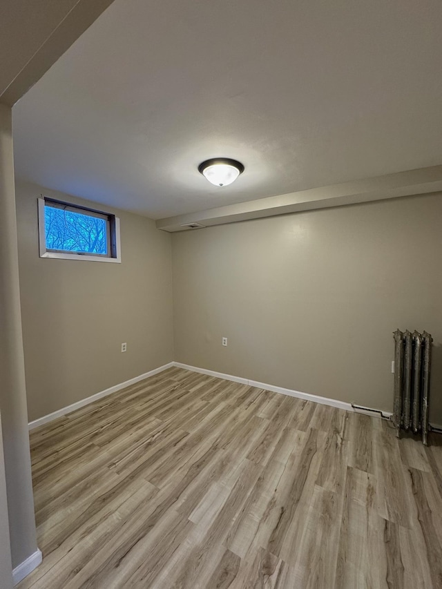 empty room with light wood-type flooring, baseboards, and radiator heating unit