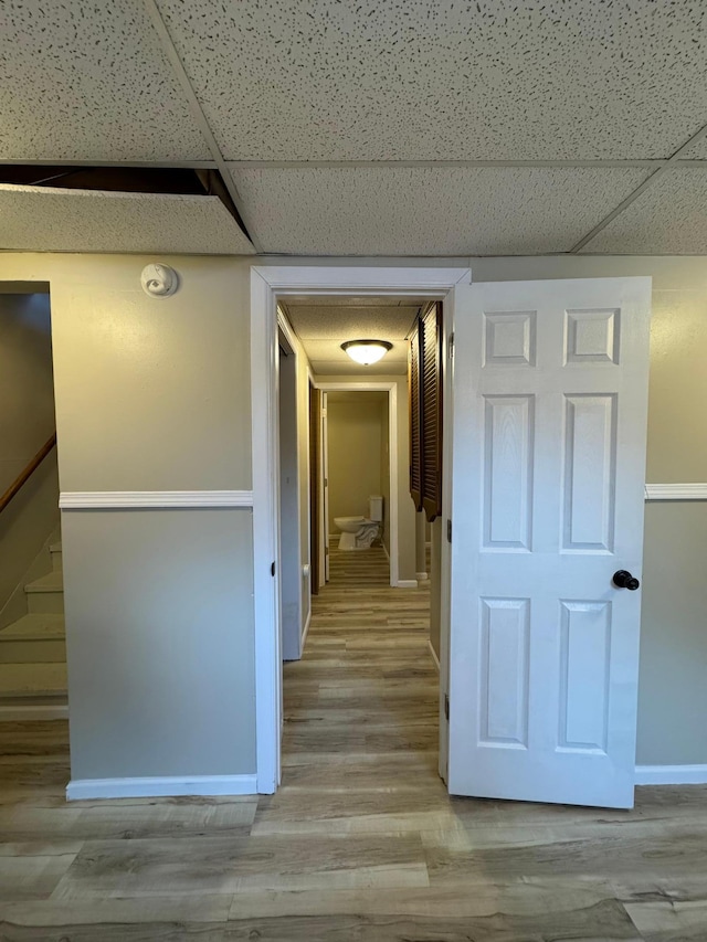 hallway featuring stairway, a drop ceiling, wood finished floors, and baseboards