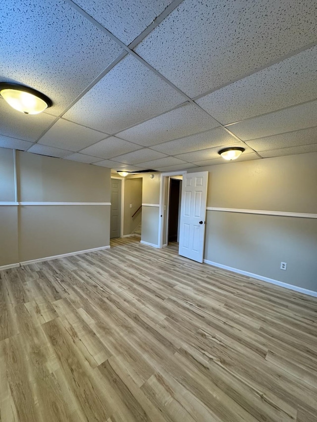 finished below grade area featuring a drop ceiling, baseboards, and wood finished floors