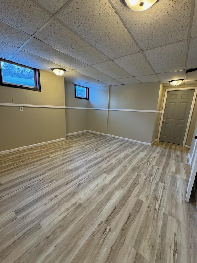 below grade area featuring a paneled ceiling, baseboards, and wood finished floors