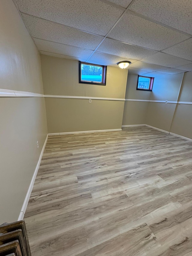 basement with a drop ceiling, plenty of natural light, baseboards, and wood finished floors