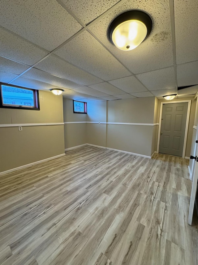 basement featuring plenty of natural light, baseboards, a drop ceiling, and wood finished floors