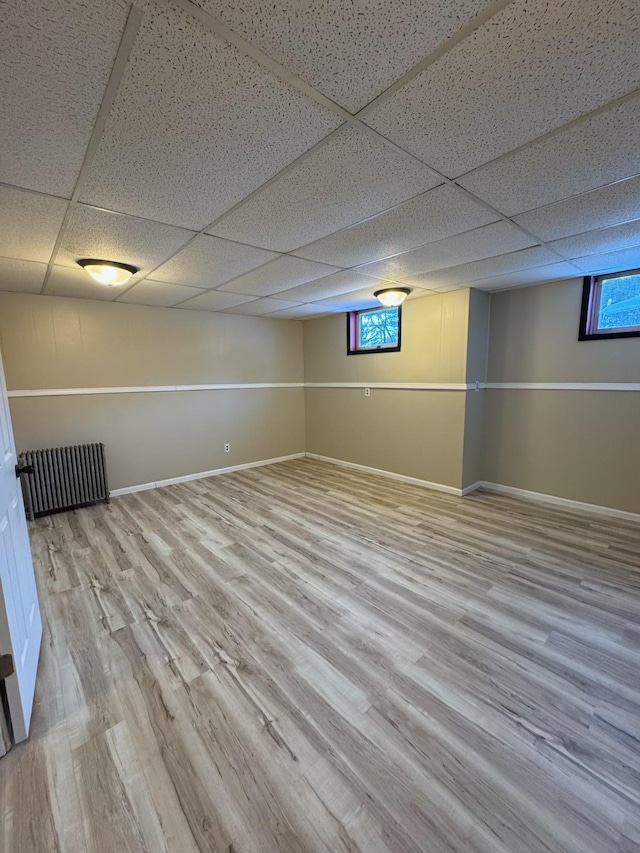 below grade area with a drop ceiling, baseboards, and wood finished floors