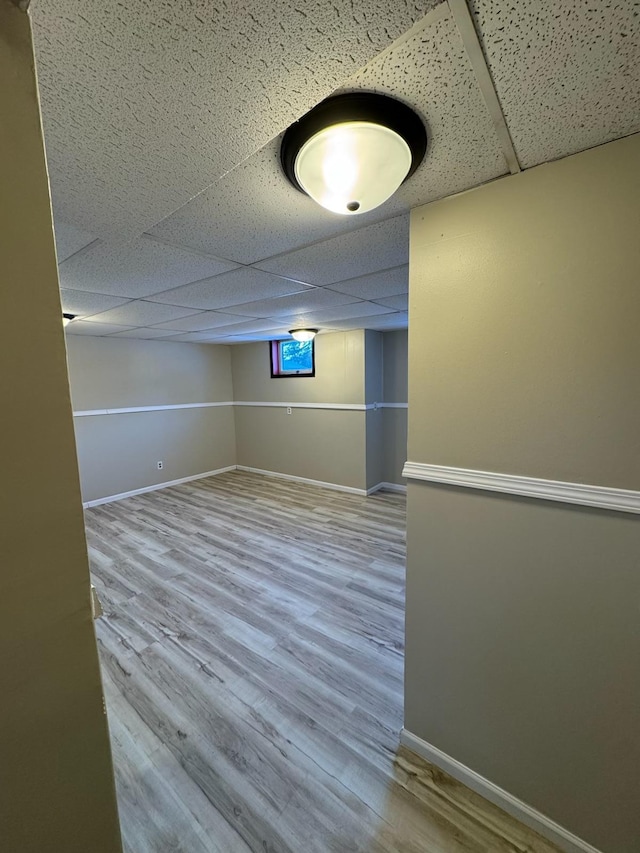 empty room featuring baseboards, a drop ceiling, and wood finished floors