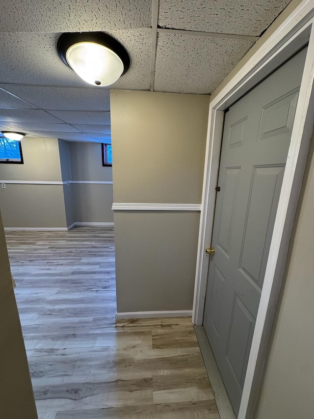 hall featuring a paneled ceiling, baseboards, and wood finished floors