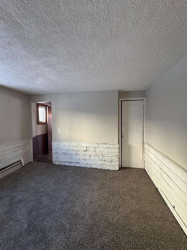 carpeted spare room with a baseboard heating unit, wainscoting, and a textured ceiling