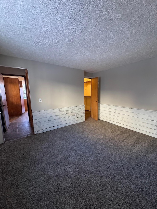 empty room with carpet floors, a wainscoted wall, and a textured ceiling