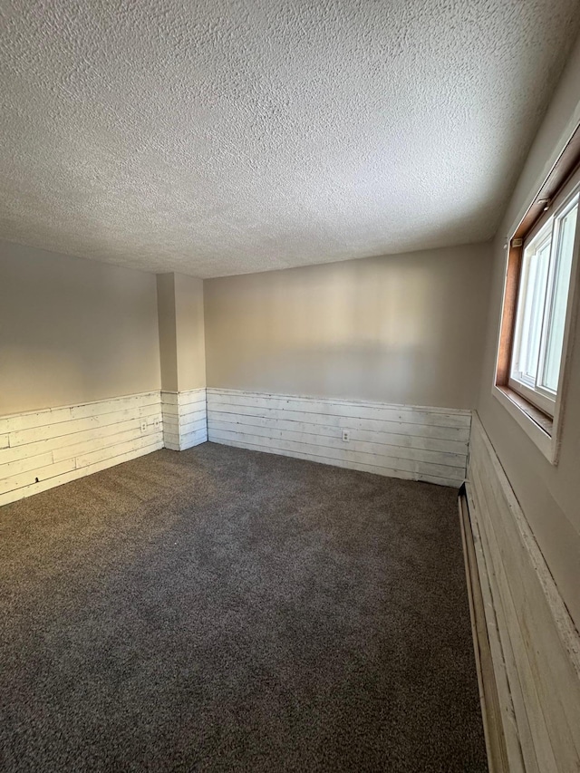 empty room with carpet, wainscoting, a textured ceiling, and a baseboard radiator