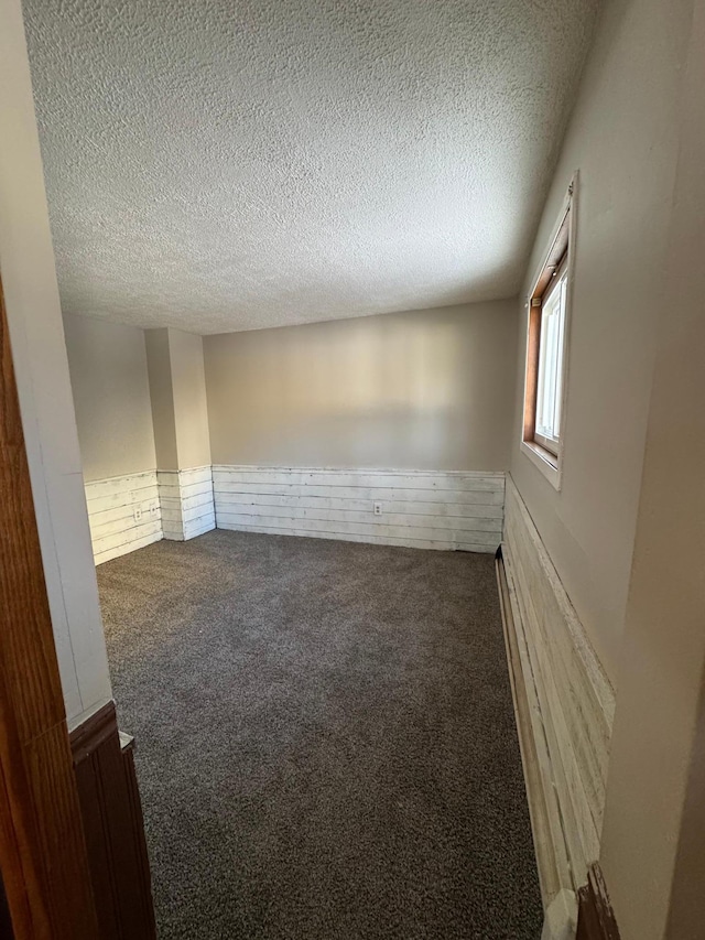 unfurnished room featuring carpet, wainscoting, and a textured ceiling