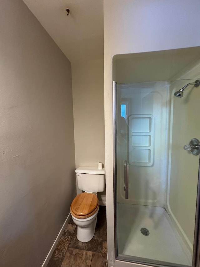 bathroom with toilet, a shower stall, and baseboards