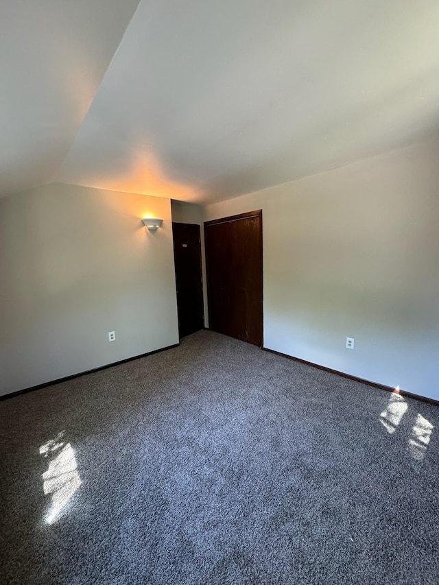 carpeted empty room featuring lofted ceiling and baseboards