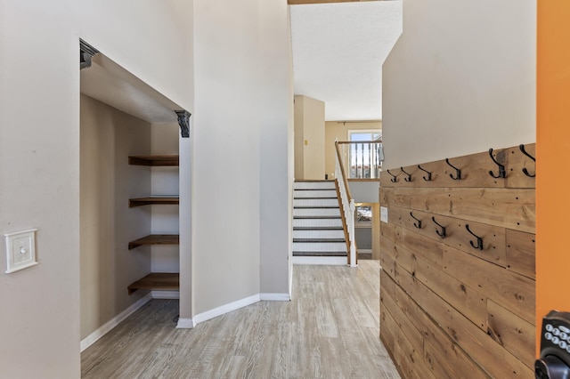 hallway featuring stairs, light wood-style flooring, and baseboards