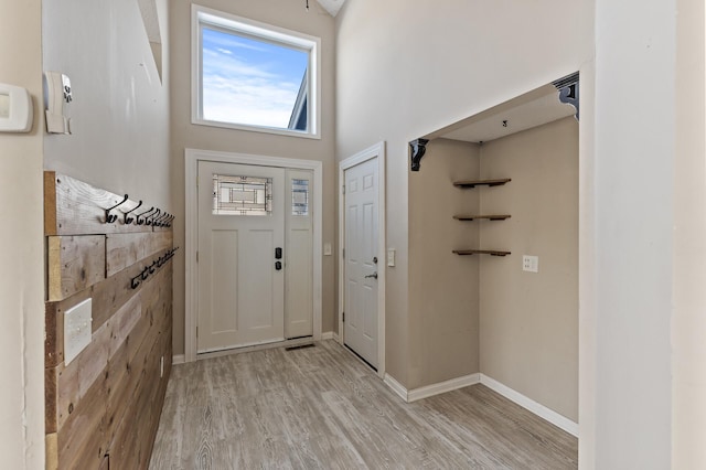 foyer featuring a towering ceiling, light wood-style flooring, and baseboards