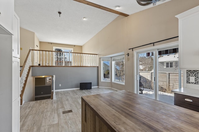 interior space featuring light wood finished floors, lofted ceiling with beams, a textured ceiling, baseboards, and stairs