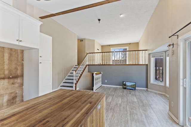 unfurnished living room with stairs, light wood-type flooring, and baseboards