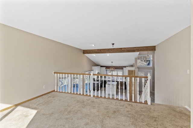 carpeted spare room with a notable chandelier, vaulted ceiling with beams, and baseboards