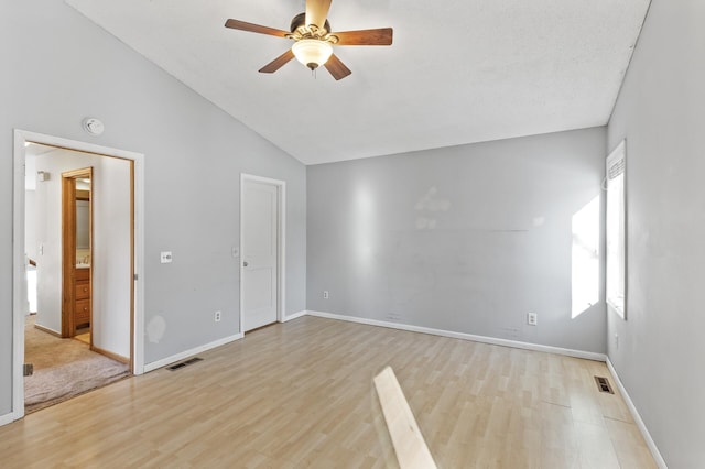 empty room with a ceiling fan, light wood-type flooring, visible vents, and vaulted ceiling