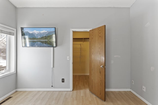 unfurnished bedroom featuring a walk in closet, visible vents, light wood-style flooring, and baseboards