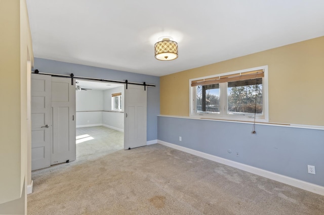 spare room featuring baseboards, a barn door, plenty of natural light, and light colored carpet