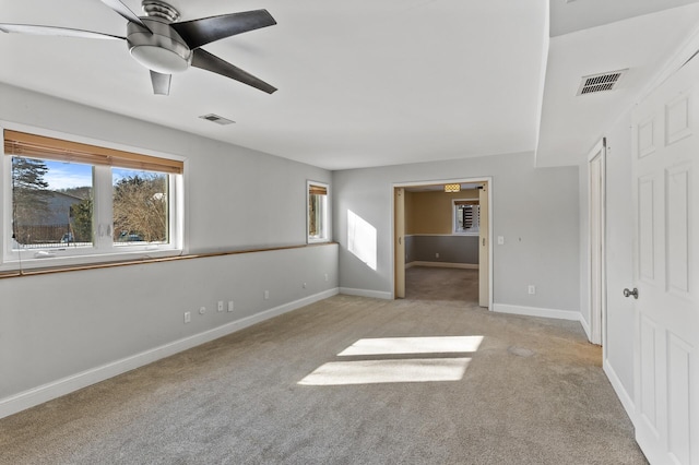 spare room with light carpet, ceiling fan, visible vents, and baseboards