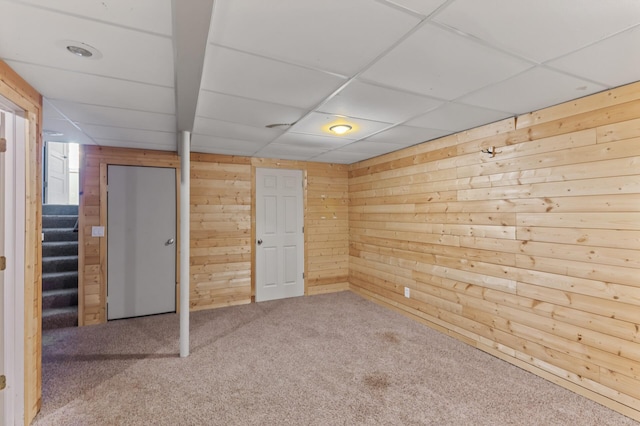 carpeted spare room featuring stairway, a drop ceiling, and wooden walls