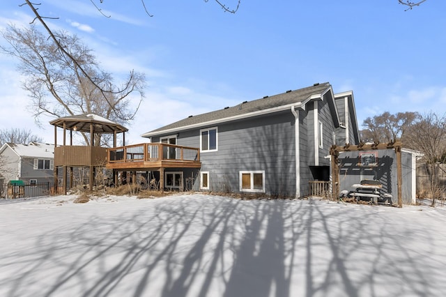 snow covered house with a deck, a gazebo, and fence