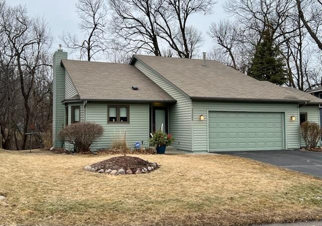 view of front facade featuring driveway, a chimney, a garage, and a front yard