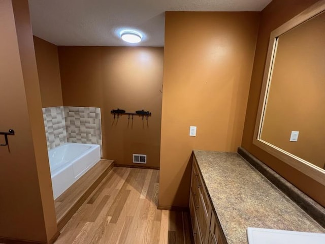 bathroom with vanity, wood finished floors, visible vents, baseboards, and a garden tub