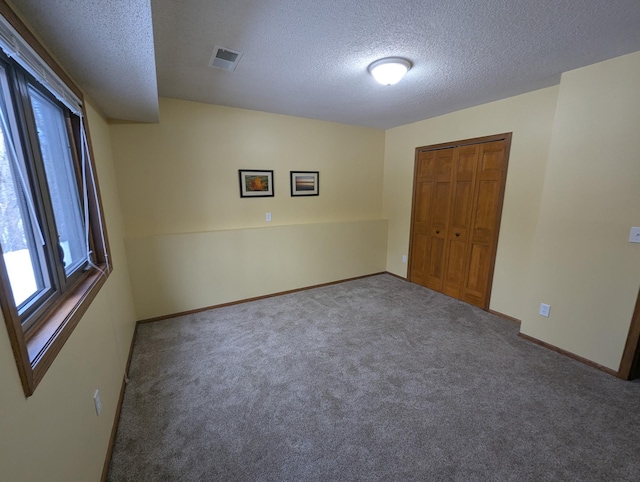 carpeted empty room featuring visible vents, a textured ceiling, and baseboards