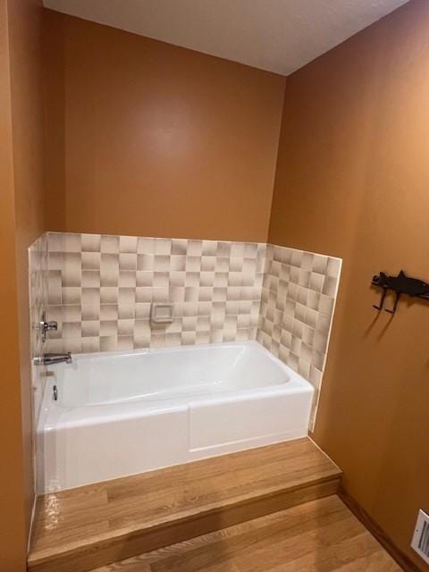 bathroom with a bath, visible vents, baseboards, and wood finished floors