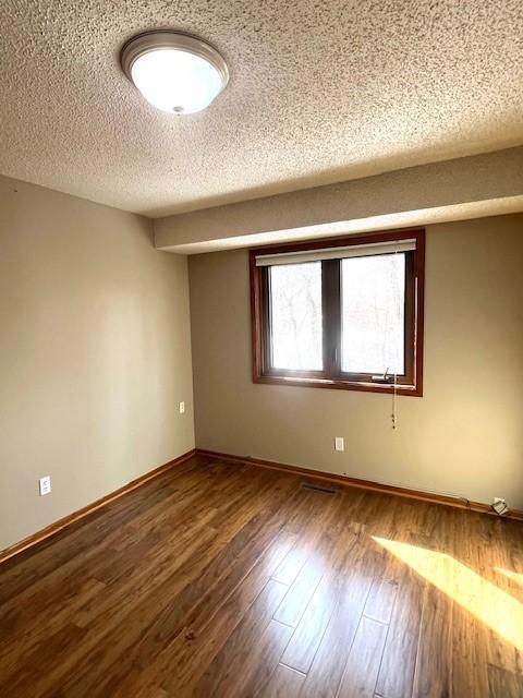 unfurnished room featuring baseboards, a textured ceiling, and wood finished floors