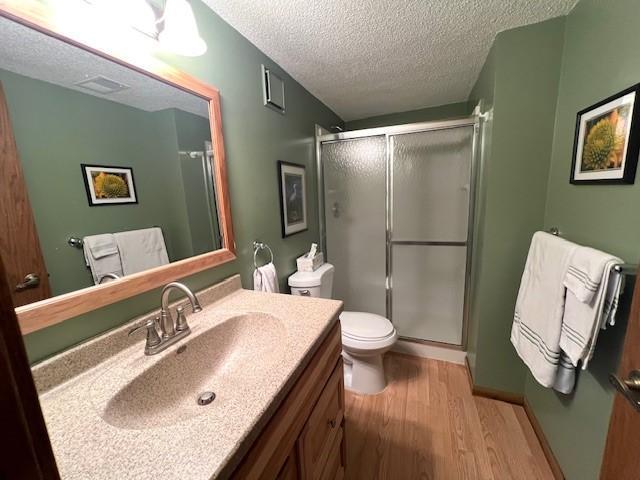 full bathroom featuring toilet, a textured ceiling, wood finished floors, a shower stall, and vanity