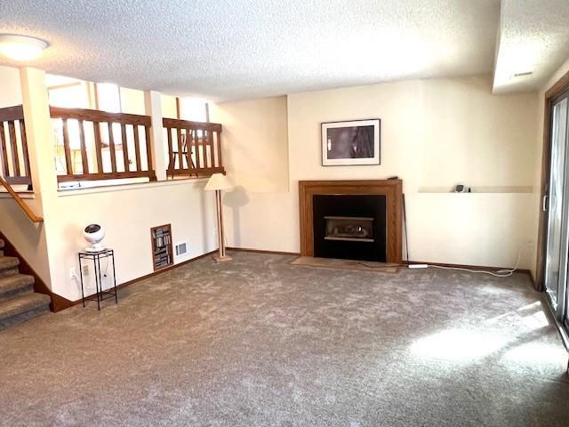 unfurnished living room with stairs, a fireplace with flush hearth, carpet, and a textured ceiling