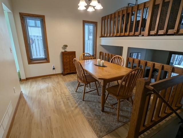 dining area with visible vents, a notable chandelier, wood finished floors, baseboards, and stairs