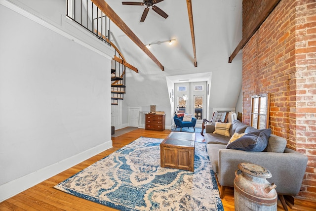 living room with ceiling fan, light hardwood / wood-style flooring, beamed ceiling, and a high ceiling