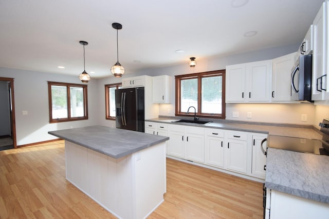 kitchen featuring sink, black fridge, white cabinetry, decorative light fixtures, and a center island