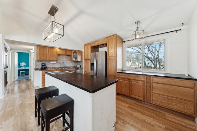 kitchen featuring tasteful backsplash, dark countertops, light wood-style flooring, a center island, and stainless steel appliances