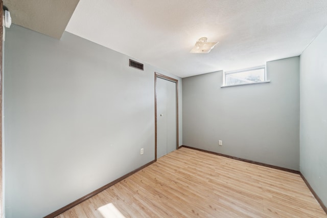 unfurnished room with a textured ceiling, wood finished floors, visible vents, and baseboards