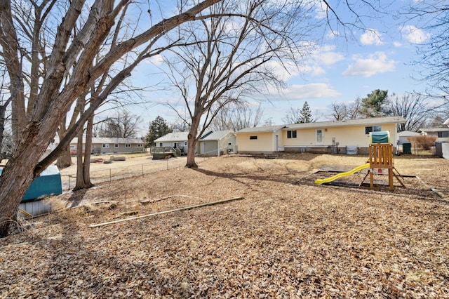 rear view of property featuring a playground and fence