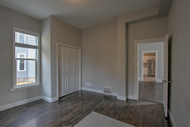 unfurnished bedroom featuring dark hardwood / wood-style floors, stainless steel refrigerator, and a closet