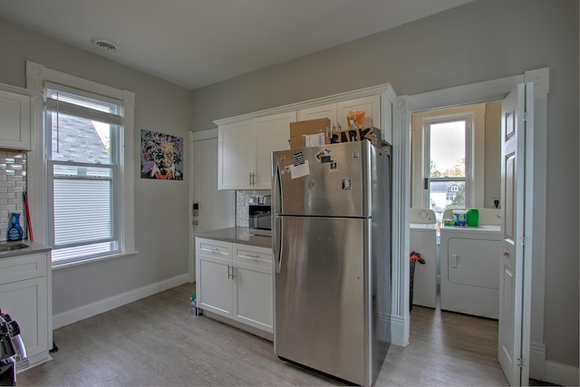 kitchen with white cabinets, stainless steel fridge, independent washer and dryer, and light hardwood / wood-style floors