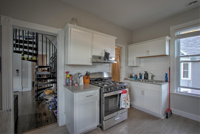 kitchen featuring stainless steel range with gas cooktop, sink, white cabinets, and backsplash