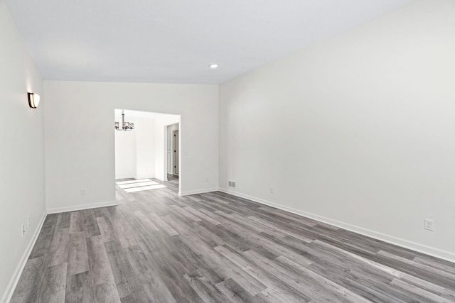 empty room with lofted ceiling, a notable chandelier, baseboards, and wood finished floors